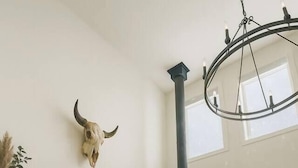 A cozy living room with a wood-burning stove, a large painting of a mountainous landscape, and a cow skull decoration on the wall.