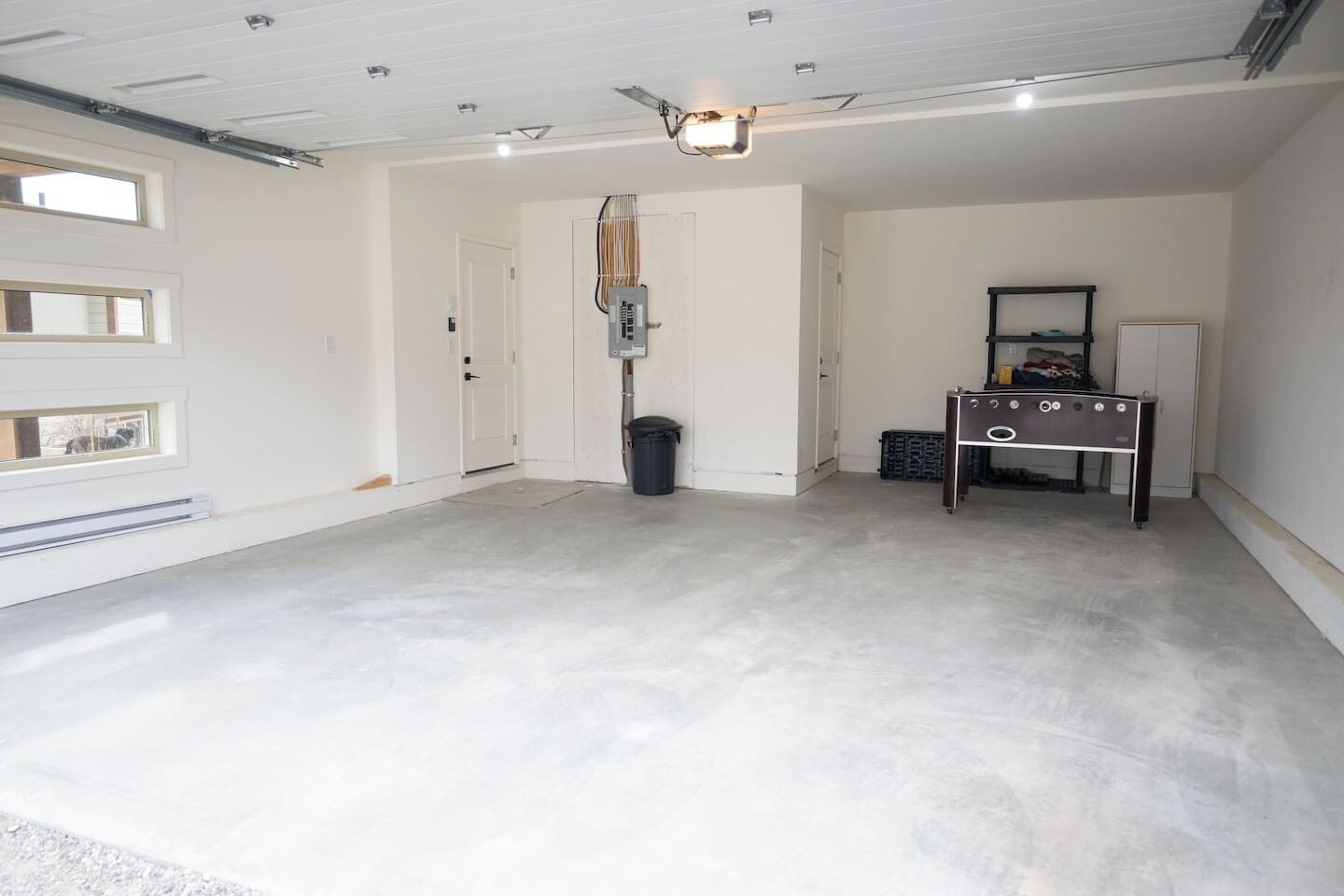 A spacious garage with a concrete floor, a ceiling fan, a workbench, and a door.