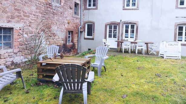 A courtyard with a wooden table and chairs, a brick wall, and a white building with windows. - La Bretz'elle, country house in the Vosges du Nord Natural Park (Lohr)