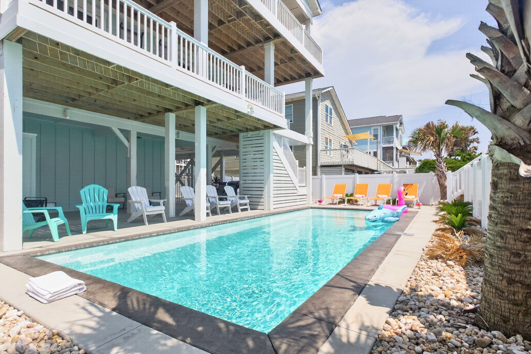 A swimming pool with lounge chairs, a covered patio, and a view of a residential building.