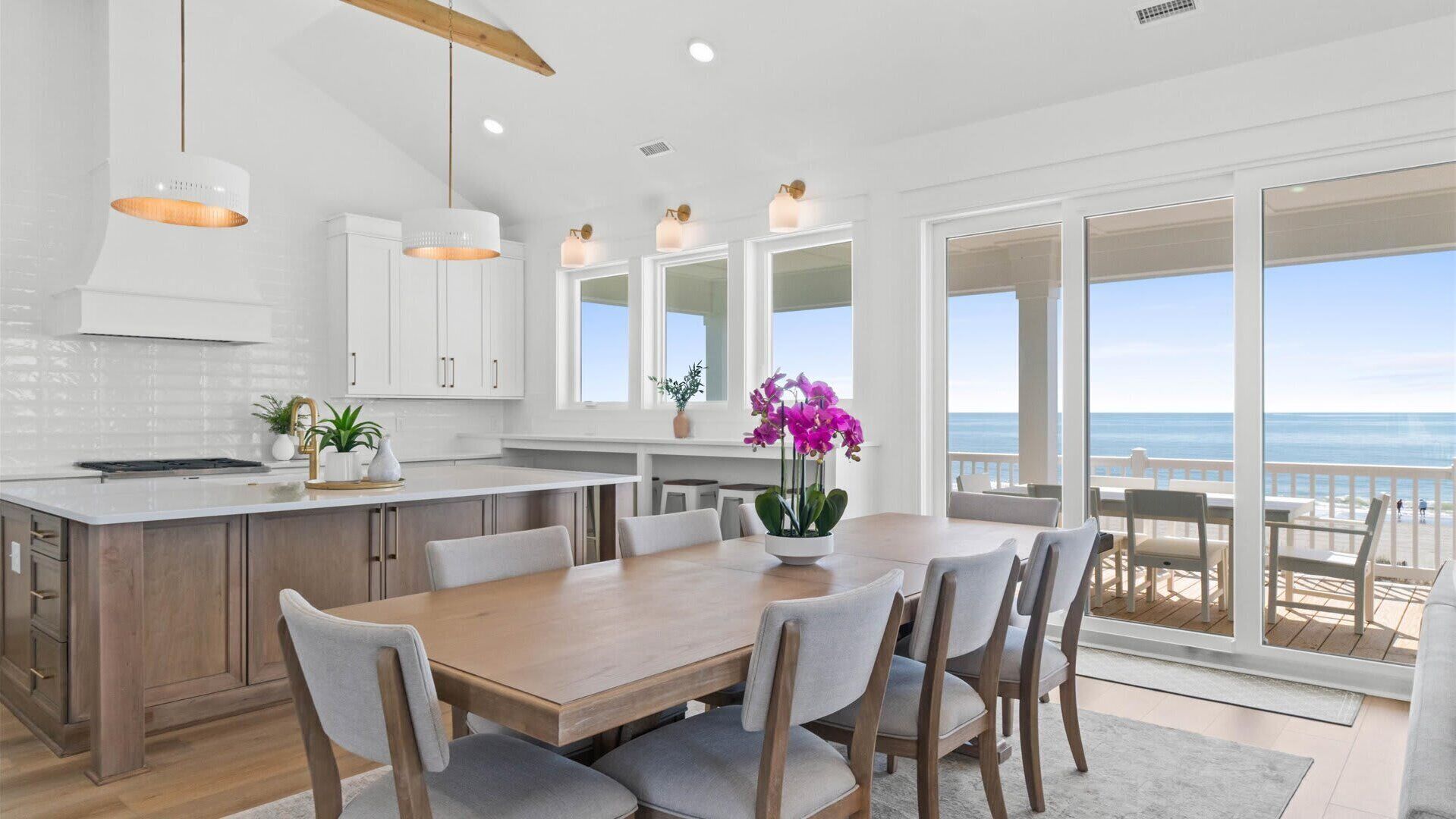 A modern kitchen with white cabinets, a wooden island, and a dining area with a view of the ocean.