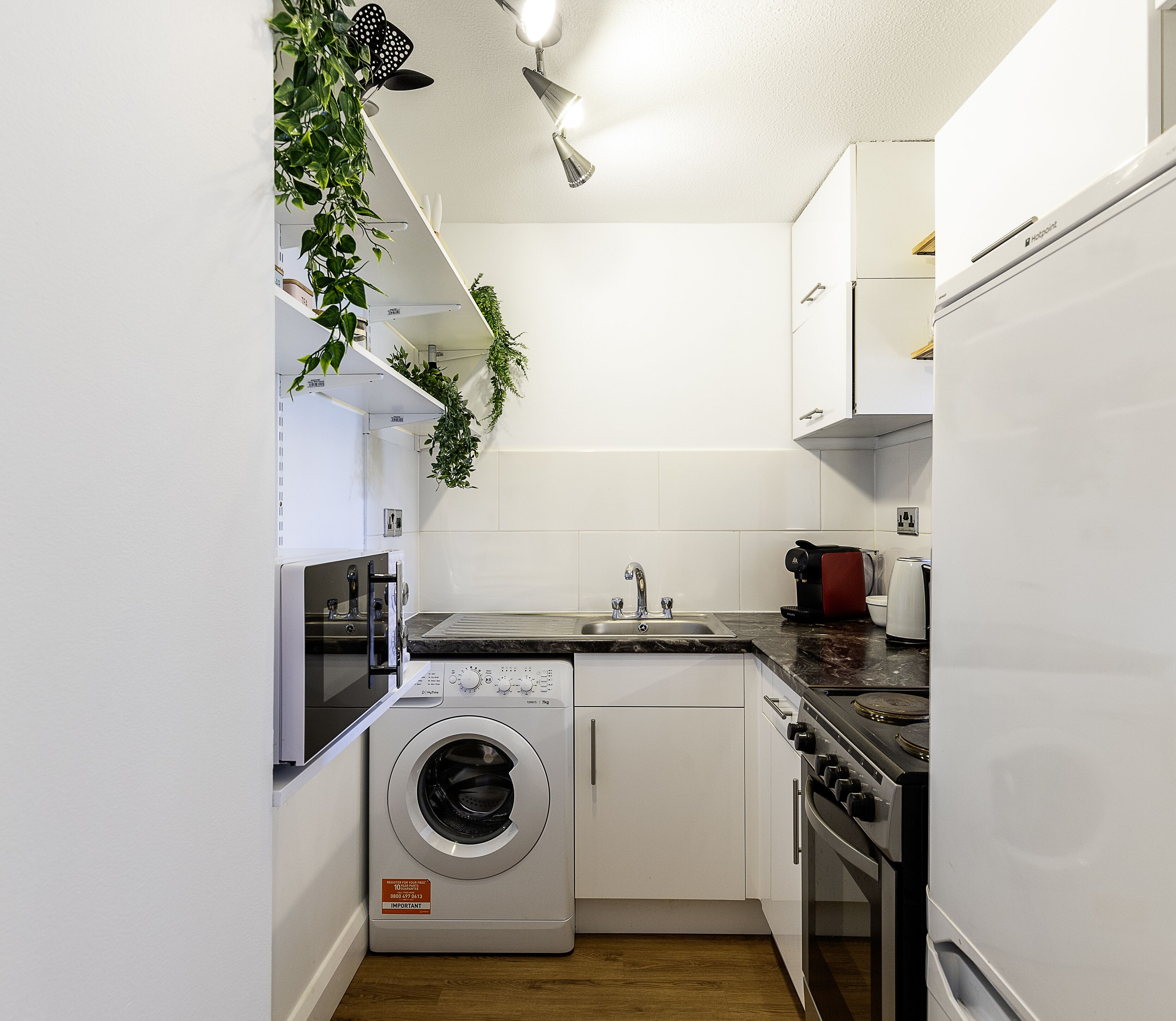 Una cocina compacta equipada con lavadora, horno, microondas y un lavabo.