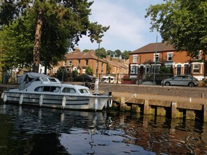 A boat docked at a pier with residential buildings in the background. - Stay Norwich Apartments Riverside AH Apartment-1 (Norwich)