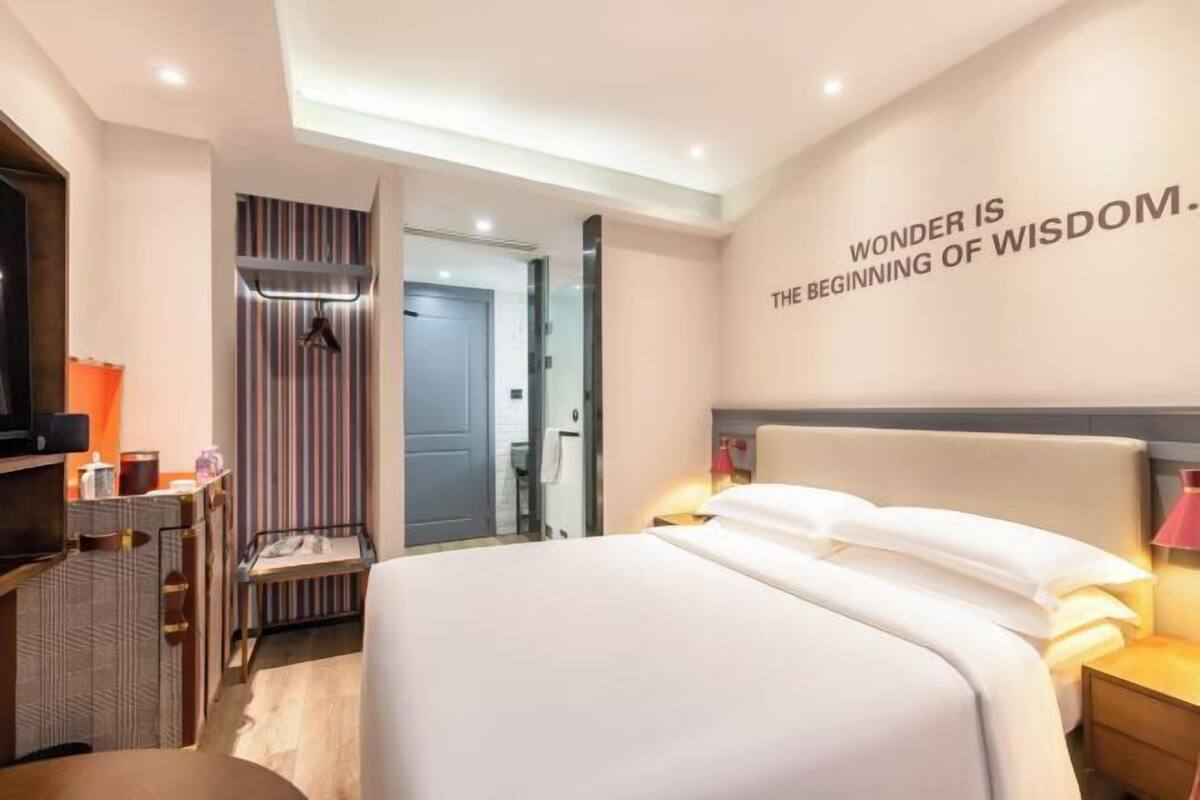 Ein modernes Hotelzimmer mit einem großen Bett, Nachttischen, einem Kleiderschrank und einem motivierenden Zitat an der Wand.