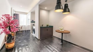 A modern hotel room with a dark wood floor, a round table with a plant, and a kitchen area with cabinets and a sink. - City Comfort Premier Hotel (Bozhou Weiwu Plaza) (Bozhou)
