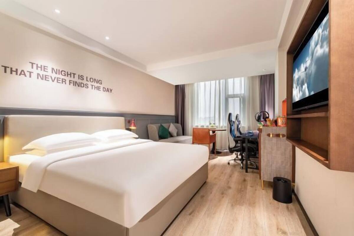 Ein Hotelzimmer mit einem großen Bett, einem Schreibtisch, einem Stuhl, einem Fernseher und einer Wand mit motivierenden Texten.