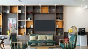 A modern living room with a green sofa, two armchairs, a coffee table, and a bookshelf filled with books and decorative items. - City Comfort Premier Hotel (Bozhou Weiwu Plaza) (Bozhou)