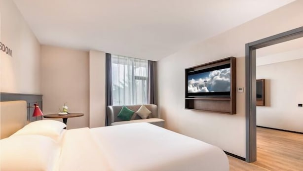 A modern hotel room with a large bed, a TV mounted on the wall, a small table with a lamp, and a window with curtains. - City Comfort Premier Hotel (Bozhou Weiwu Plaza) (Bozhou)