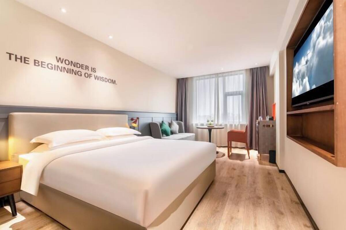 Ein modernes Hotelzimmer mit einem großen Bett, einem Fernseher, einem Schreibtisch und einer Wand mit motivierenden Texten.