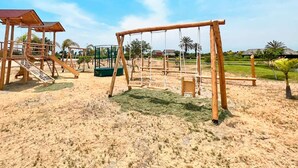 A playground with swings and slides, surrounded by sand and greenery. - HOP Munay Relajante en Campo y Playa en Chincha (El Carmen)