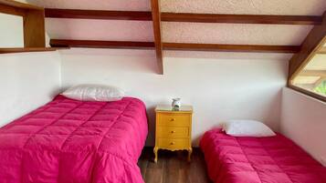 A small, well-lit room with two beds, a wooden nightstand, and a window.