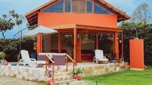 A modern house with a sloped roof, large glass windows, and a covered patio area with outdoor seating. - HOP Munay Relajante en Campo y Playa en Chincha (El Carmen)