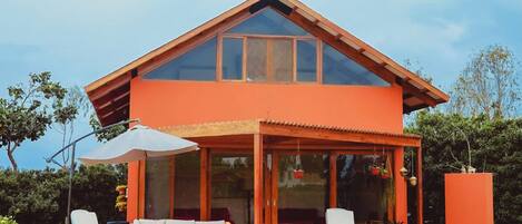 Una casa moderna con techo inclinado, grandes ventanas de vidrio y un patio cubierto con mobiliario exterior.