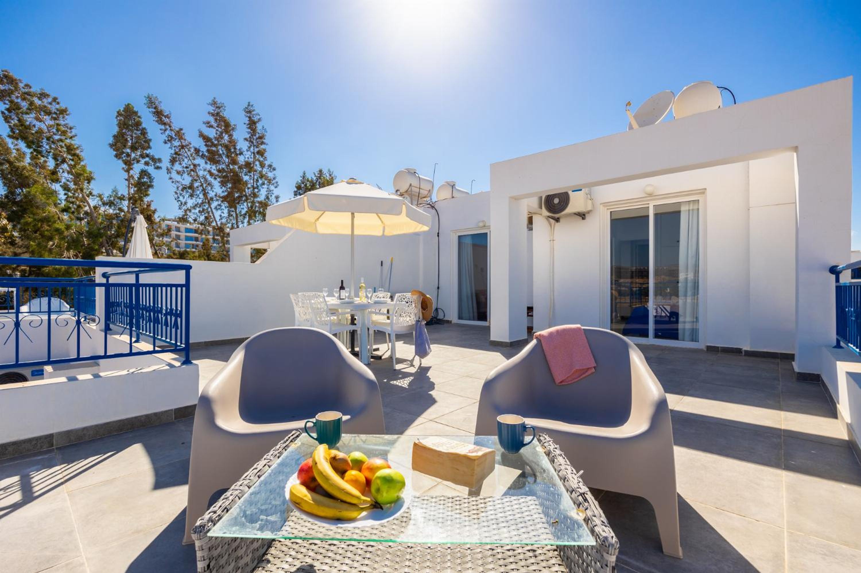 A rooftop terrace with a table set for two, a fruit bowl, and a glass table.