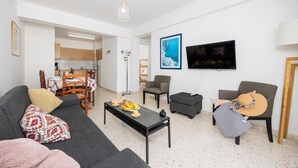 A modern living room with a sofa, coffee table, and chairs. A dining area is visible in the background.
