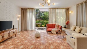 A modern living room with a TV, sofas, a patterned rug, and a large window with curtains. - Stylish 2BR w Pool Near Candolim and Coco Beach (Verem)