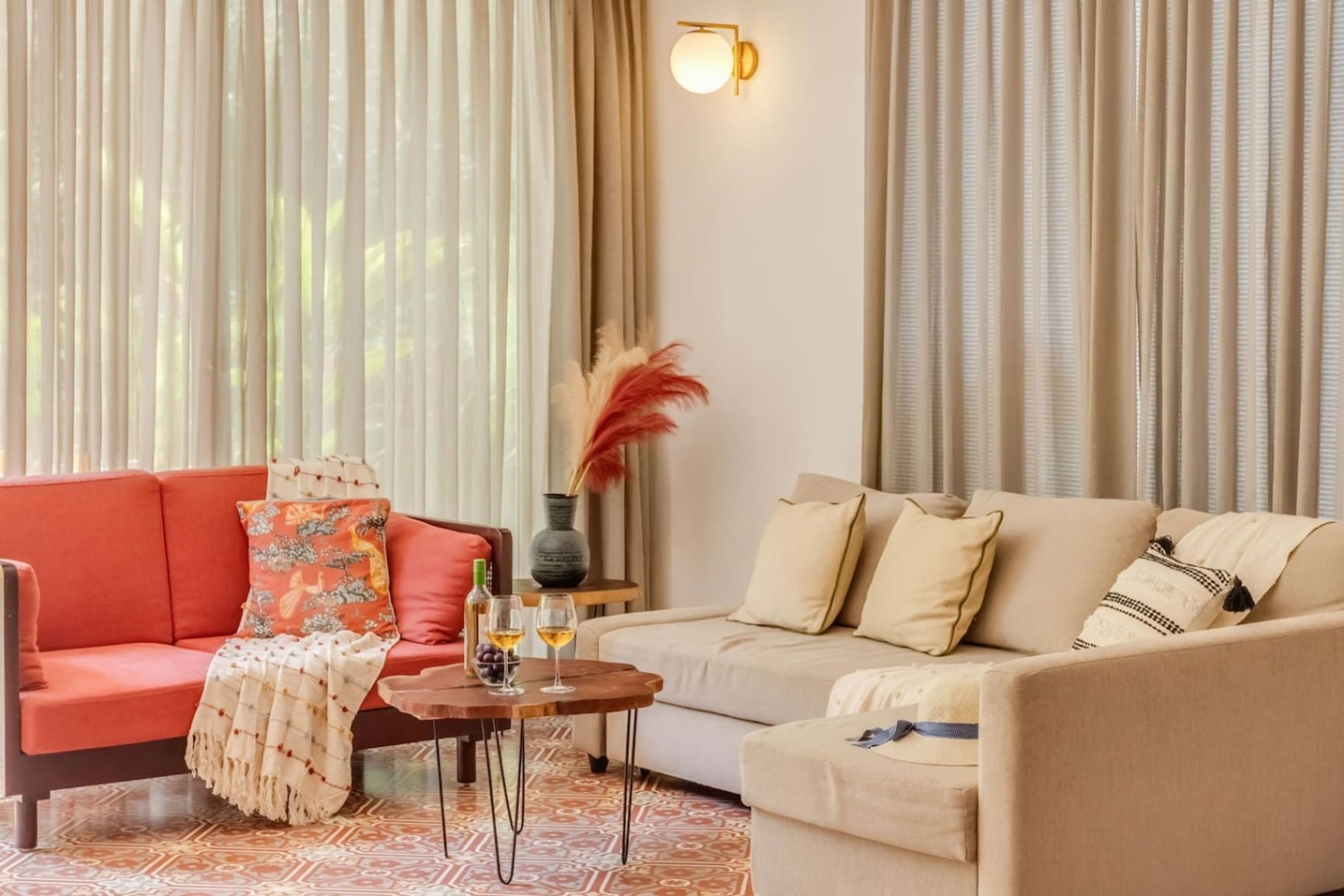 A living room with a red sofa, a beige sofa, a coffee table with wine glasses, and a vase with dried plants.