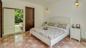A bedroom with a bed, a nightstand, a wall-mounted light, a ceiling fan, and a door leading to a balcony. - Stylish 2BR w Pool Near Candolim and Coco Beach (Verem)
