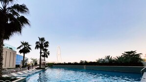 A swimming pool with palm trees and a Ferris wheel in the background. - Elegant Address JBR 3BR w Beach Accesss (Dubai)