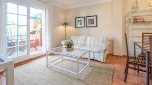 A living room with a white sofa, a glass coffee table, a floor lamp, and a bookshelf. - Isla Canela Golf in Isla Canela (Ayamonte)