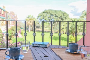 Une table avec un livre, deux tasses et un verre d’eau, sur un balcon donnant sur un terrain de golf.