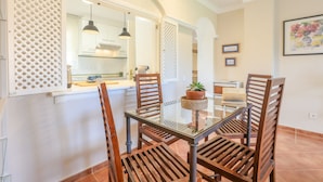 A dining area with a glass table, wooden chairs, a potted plant, and a kitchen in the background. - Isla Canela Golf in Isla Canela (Ayamonte)
