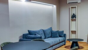 A modern living room with a blue sofa, two chairs, a round table, and a white wall with an air conditioning unit. - Downtown Zadar Stylish and Sophisticated Apartments (Zadar)