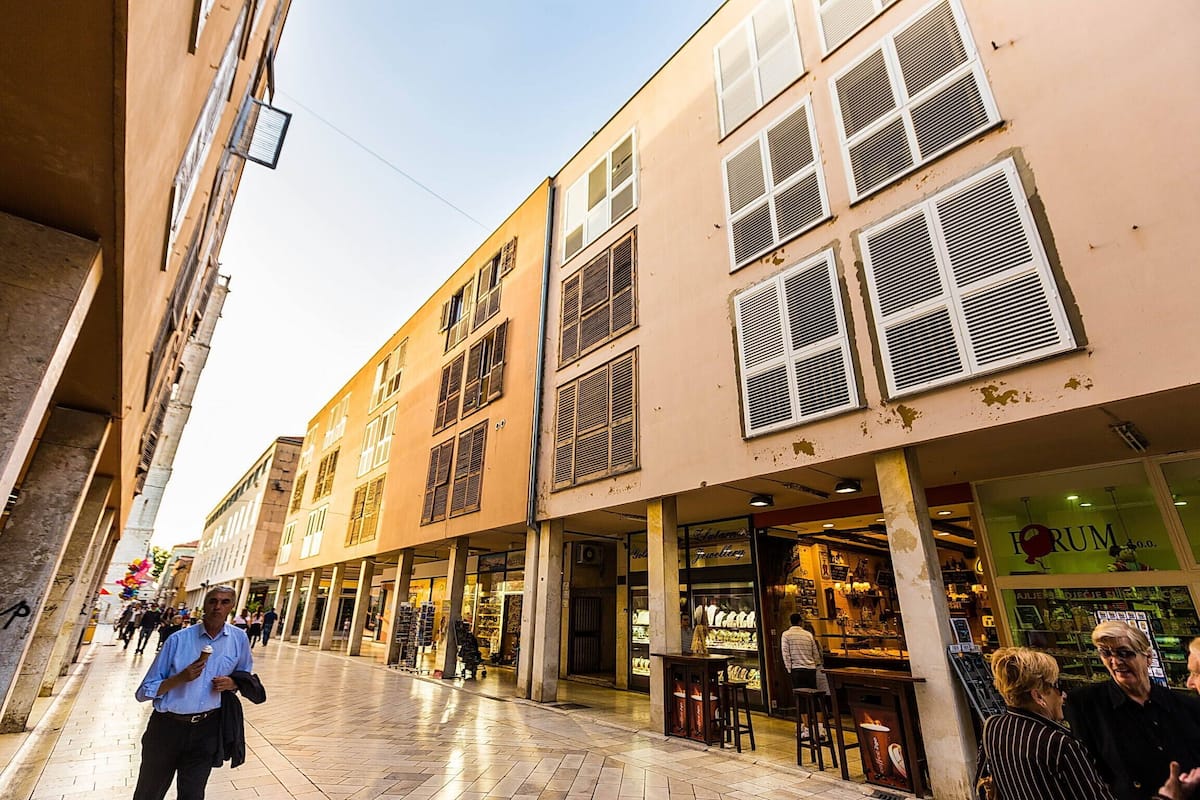 Une rue bordée d’immeubles, de boutiques et où l’on voit des gens qui se promènent.