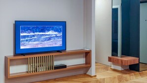 A modern living room with a flat-screen TV on a wooden console, a large mirror, and a wooden floor. - Downtown Zadar Stylish and Sophisticated Apartments (Zadar)