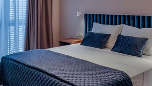 A neatly made bed with a dark blue quilt, a headboard with vertical panels, and a wooden nightstand beside it. - Downtown Zadar Stylish and Sophisticated Apartments (Zadar)