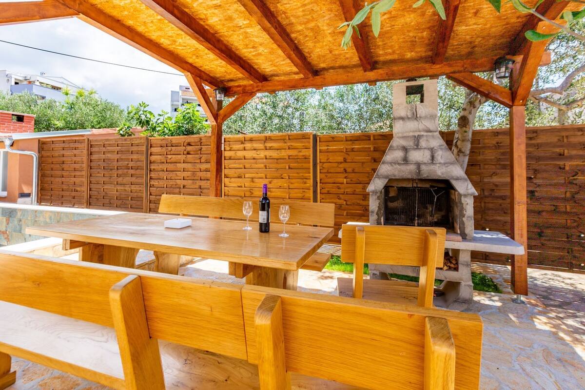 An outdoor patio with wooden furniture, a stone fireplace, and a brick wall.