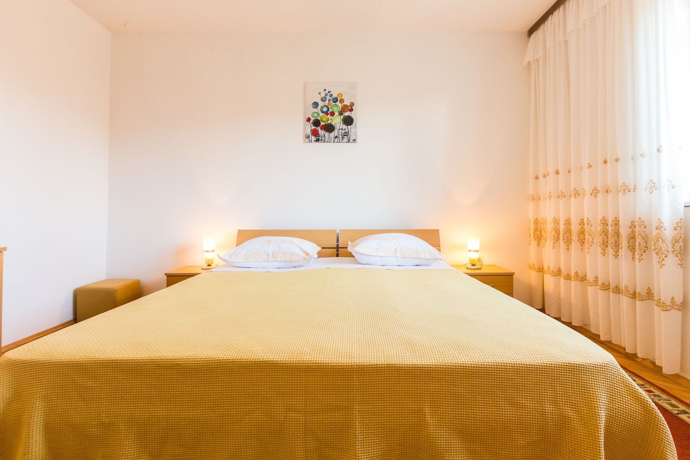 A hotel room with a large bed, two bedside tables with lamps, a wall-mounted artwork, and a curtain with a pattern.