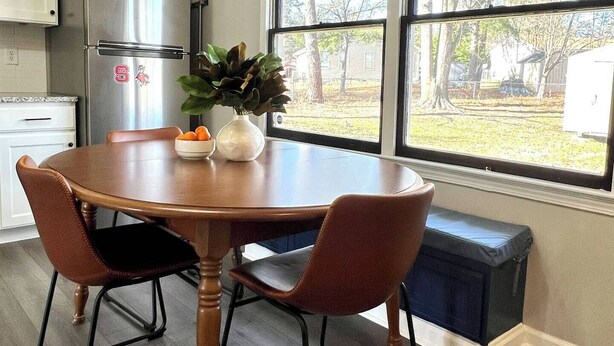 A kitchen with a wooden table, two chairs, a refrigerator, and a window with a view of the outdoors. - Ranch Home on Quiet Court Between Raleigh and Garner (Garner)