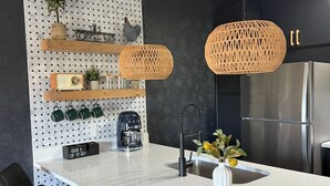 Cocina moderna con una isla blanca, sillas negras, un refrigerador de acero inoxidable y un panel perforado con varios objetos.