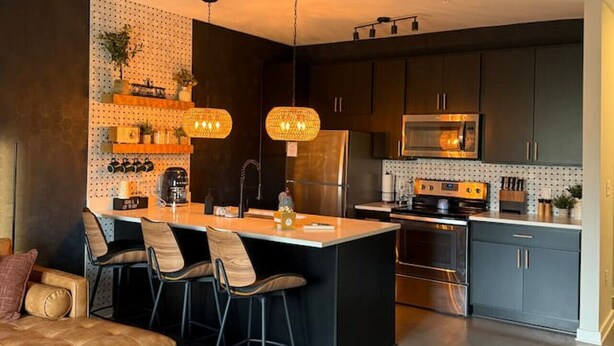 Una cocina moderna con una isla central, armarios oscuros e iluminación colgante.