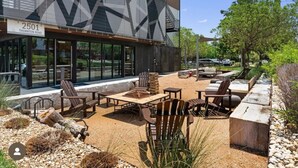 Un patio exterior con asientos, un pozo de fuego y un edificio con fachada geométrica y un letrero que dice "2501 Thornton Road".