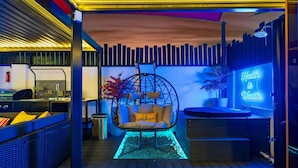 Un espacio al aire libre moderno con una silla colgante, un letrero de neón y una zona de bar.