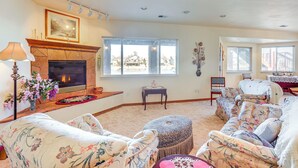 A living room with a fireplace, floral-patterned furniture, and large windows offering a view of the outside. - 7 Mi to Dtwn Denver: Lakefront Gem w/ Dock! (Denver)