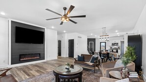 A modern living room with a flat-screen TV, a fireplace, a ceiling fan, and a dining area in the background. - 7 min to Wild Turkey and Four Roses - Sleeps 10 - Patio with Grill and View (Lawrenceburg)