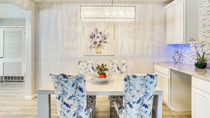 A dining area with a white table, floral chairs, a chandelier, and a wall-mounted vase. - Patio & Fenced Yard: Newly Renovated Hurst Home! (Hurst)