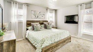 A bedroom with a wooden bed, white curtains, a flat-screen TV, and a painting on the wall. - Patio & Fenced Yard: Newly Renovated Hurst Home! (Hurst)