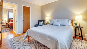 Un dormitorio con una cama grande, dos lámparas de noche, una puerta de madera y una alfombra estampada.