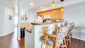 A modern kitchen with wooden cabinets, a microwave, and a bar area with patterned chairs. - 5th Fl Lakefront Condo: Elevator, Pool, Boat Slip! (Osage Beach)