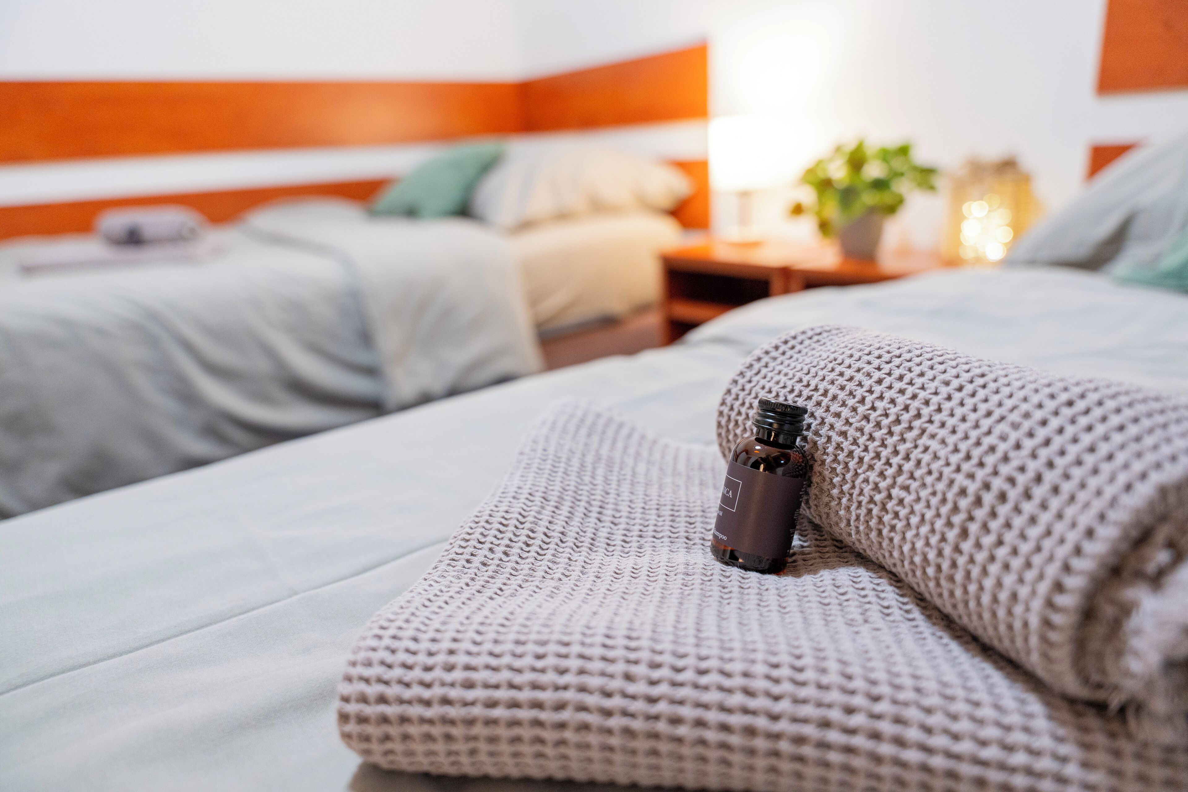 A neatly made bed with a rolled towel and a bottle of lotion.