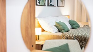 Un dormitorio con cama, almohadas, una mesita de noche con lámpara y una pared decorada con marcos.