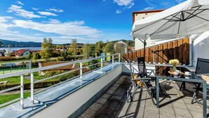Una terraza en la azotea con vistas a un lago, una valla de madera y una mesa con sillas.