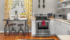 A modern kitchen with a stainless steel oven, a microwave, and a dining area with stools. - The Cushman House B: Unit B near 6th Ave UPS UW Ruston (Tacoma)