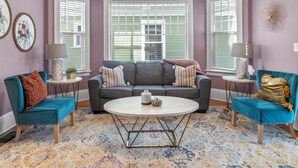 A living room with a grey sofa, teal armchairs, a round coffee table, and a floral patterned rug. - The Cushman House B: Unit B near 6th Ave UPS UW Ruston (Tacoma)