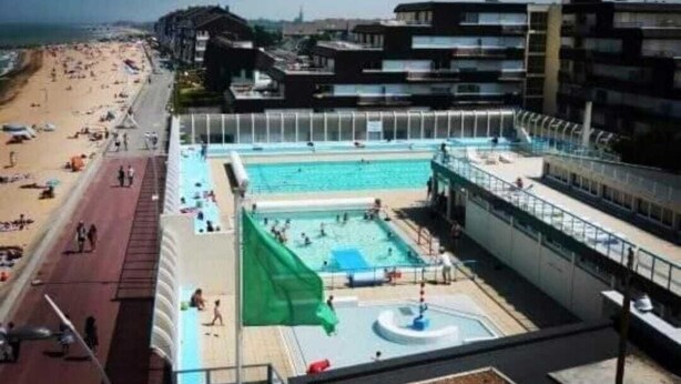 Zona de piscina en la azotea con vistas a la playa y edificios al fondo.