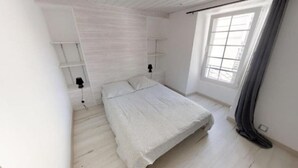 Un dormitorio con cama, ventana con cortinas y estanterías empotradas.